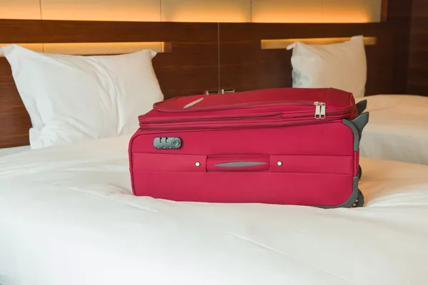 Červený kufr na posteli v hotelovém pokoji — Stock fotografie