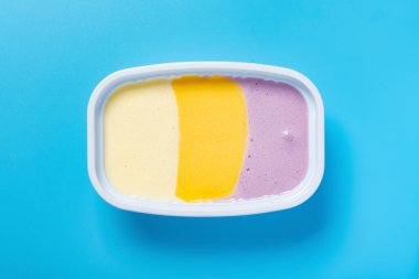 Mavi arka planda erimiş bir fincan çok renkli dondurma.