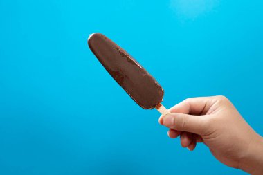 Adam mavi arka planda taze çikolatalı buzlu dondurma tutuyor.