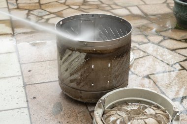 Yüksek basınçlı bir silahla bir çamaşır makinesinin dışını temizlemek.