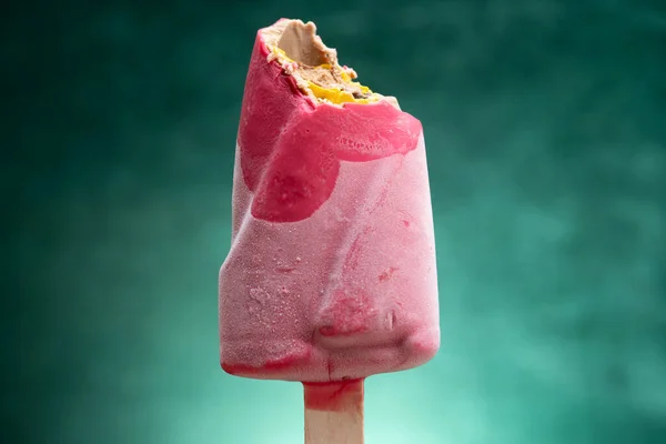 pink color chocolate outer popsicle with some bites on a gradient green background