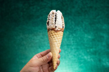 Vanilya ve çikolata aromalı dondurma külahını yeşil bir zeminde tutan el.