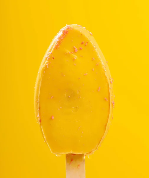 巧克力外层黄色冰棒在黄色背景下开始在垂直组合中融化 — 图库照片