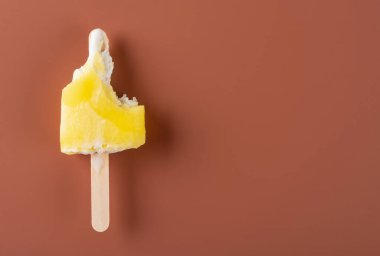 mostly eaten yellow popsicle on a brown background