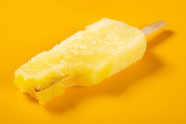 angle view orange color popsicle with some bites on an orange color background