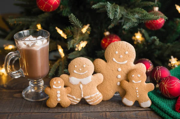 Gingerbread men with a cup of cocoa, marshmallows on a wooden table with Christmas lights and decorations.