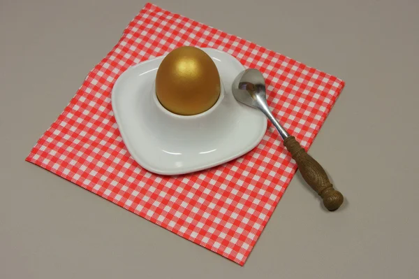 Golden egg in an egg cup on a red patterned napkin with spoon — Stock Photo, Image