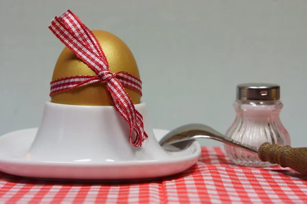 Golden egg in an egg cup on a red patterned napkin — Stock Photo, Image