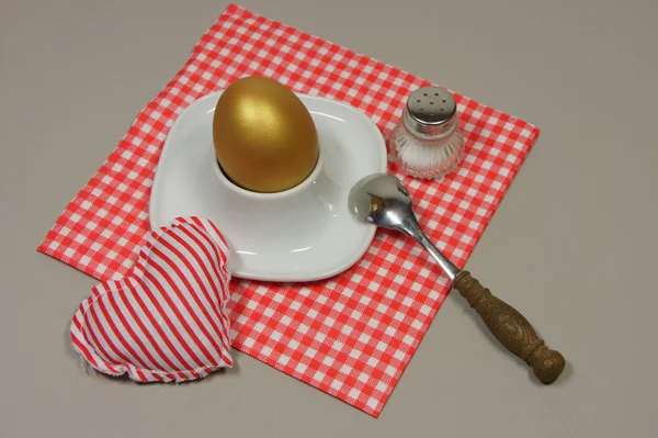 Golden egg in an egg cup on a red patterned napkin — Stock Photo, Image