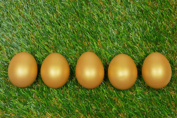 Five golden eggs on a green artificial turf — Stock Photo, Image