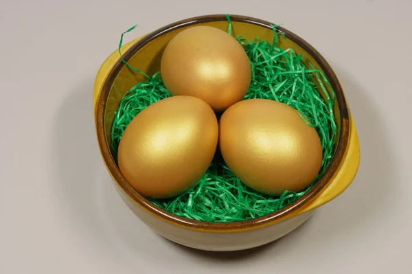 Three golden eggs in a bowl on green grass — Stock Photo, Image