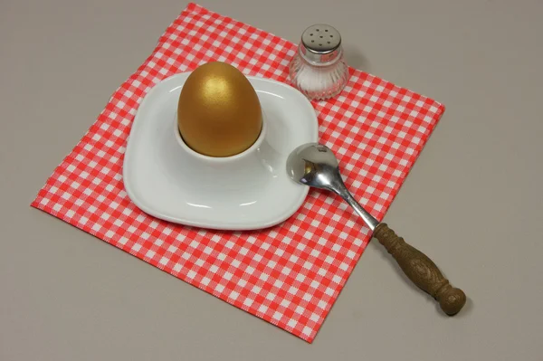 Golden egg in an egg cup on a red patterned napkin — Stock Photo, Image