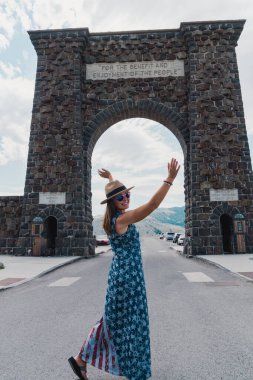 Yellowstone Ulusal Parkı 'ndaki Theodore Roosevelt Kemeri önünde Amerikan bayrağı ve şapkası giymiş vatansever bir kadın poz veriyor.