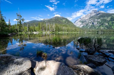 Grand Teton Ulusal Parkı 'ndaki Taggart Gölü, güneşli ve sakin bir sabahta kayaların çerçevelediği yer.