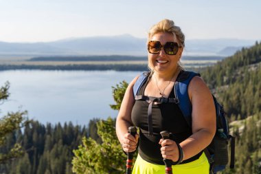 Blonde hiker woman poses at Inspiration Point in Grand Teton National Park, overlooking Jenny Lake