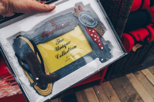 Calgary, Alberta, Canada - July 16, 2022: Hand holds up a picture frame with the Calgary Stampede logo at a store selling official Calgary Stampede merchandise and souvenirs