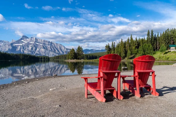 Two Jack Lake with the iconic red adirondack chairs at the shoreline in Banff National Park