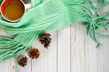 Kahve fincanı, deniz mavisi örgü eşarp ve ahşap arka planda çam kozalakları ile samimi bir sonbahar düzenlemesi.