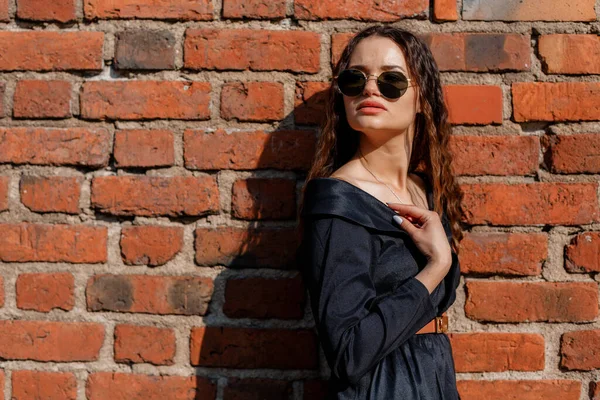 Kaliteli tüvit ceketli, gözlüklü ve başka tarafa bakan bir kız. Beyaz tuğla duvarın yanında güneş gözlüğü takan bir kız. Varşova.