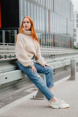 Şehirdeki yolda oturan kızıl saçlı kız. Güzel bir şehrin sokaklarında güzel bir kızın portresi. Kızıl saçlı, çilli ve kameraya bakan olgun bir kadın..