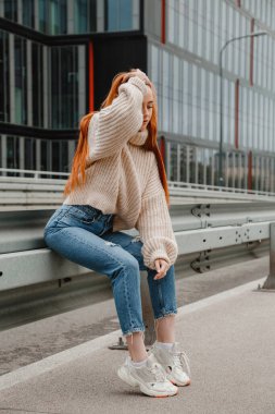 Şehirdeki yolda oturan kızıl saçlı kız. Güzel bir şehrin sokaklarında güzel bir kızın portresi. Kızıl saçlı, çilli ve kameraya bakan olgun bir kadın..