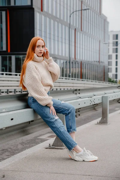 Ragazza con i capelli rossi seduta sulla strada in città. Ritratto di una bella ragazza per le strade della bella città. Donna matura con i capelli rossi e lentiggini guardando la fotocamera. — Foto Stock