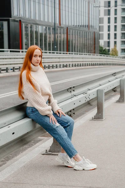 Egy vörös hajú lány ül az úton a városban. Egy gyönyörű lány portréja a gyönyörű város utcáin. Érett nő vörös haj és szeplők nézi a kamerát. — Stock Fotó