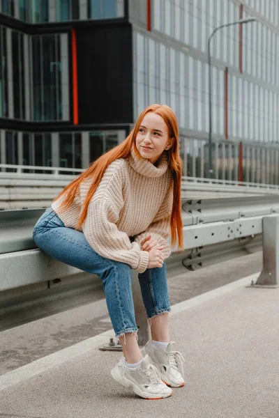 Egy vörös hajú lány ül az úton a városban. Egy gyönyörű lány portréja a gyönyörű város utcáin. Érett nő vörös haj és szeplők nézi a kamerát. — Stock Fotó
