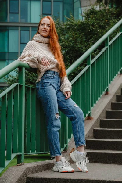 Mujer pelirroja con un atuendo elegante. Chica de estilo de moda con el pelo largo y rojo. Estilo de calle Moderna chica urbana estricta en las escaleras. — Foto de Stock