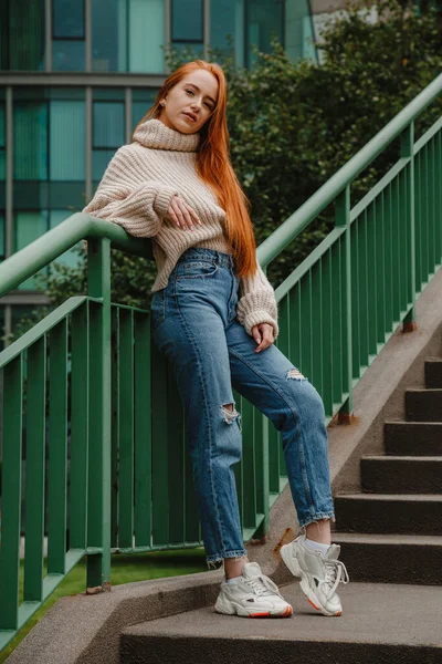 Mujer pelirroja con un atuendo elegante. Chica de estilo de moda con el pelo largo y rojo. Estilo de calle Moderna chica urbana estricta en las escaleras. — Foto de Stock