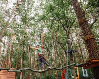 Cesur küçük çocuk macera parkında eğleniyor ve kaskla kameraya gülümsüyor. İp atma alıştırması yapan bir izci. Çocuk - bir oğlan ve bir kız halat parkında engelleri aşıyor.
