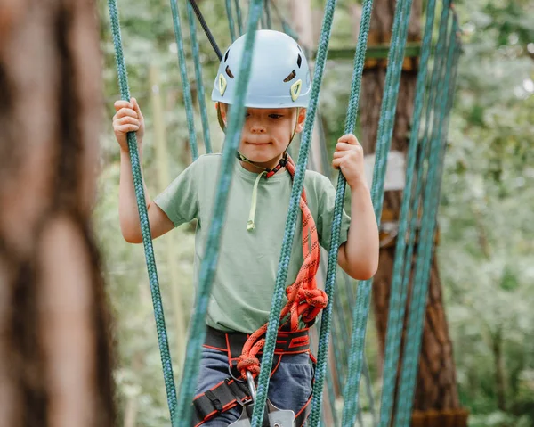 Cesur küçük çocuk macera parkında eğleniyor ve kaskla kameraya gülümsüyor. İp atma alıştırması yapan bir izci. Çocuk - bir oğlan ve bir kız halat parkında engelleri aşıyor.