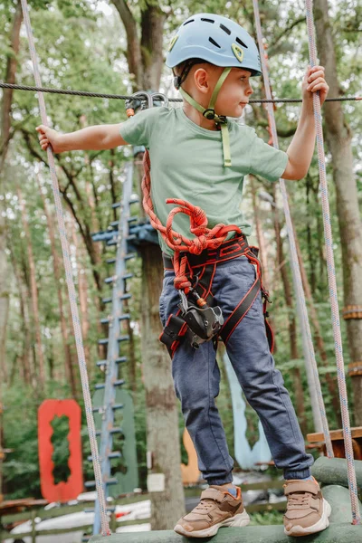 Cesur küçük çocuk macera parkında eğleniyor ve kaskla kameraya gülümsüyor. İp atma alıştırması yapan bir izci. Çocuk - bir oğlan ve bir kız halat parkında engelleri aşıyor.