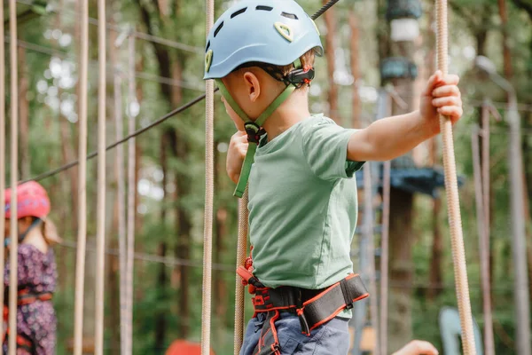 Cesur küçük çocuk macera parkında eğleniyor ve kaskla kameraya gülümsüyor. İp atma alıştırması yapan bir izci. Çocuk - bir oğlan ve bir kız halat parkında engelleri aşıyor.