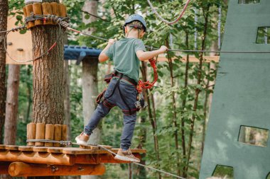 Cesur küçük çocuk macera parkında eğleniyor ve kaskla kameraya gülümsüyor. İp atma alıştırması yapan bir izci. Çocuk - bir oğlan ve bir kız halat parkında engelleri aşıyor.