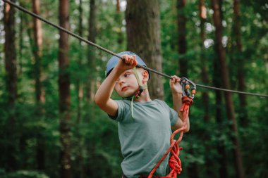 Cesur küçük çocuk macera parkında eğleniyor ve kaskla kameraya gülümsüyor. İp atma alıştırması yapan bir izci. Çocuk - bir oğlan ve bir kız halat parkında engelleri aşıyor.
