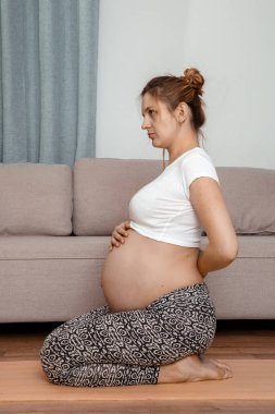 Güzel hamile kadın karnını tutarak oturuyor. Genç hamile kadın dizlerinin üstüne çöker..