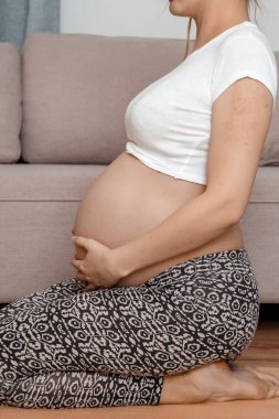 Güzel hamile kadın karnını tutarak oturuyor. Genç hamile kadın dizlerinin üstüne çöker..