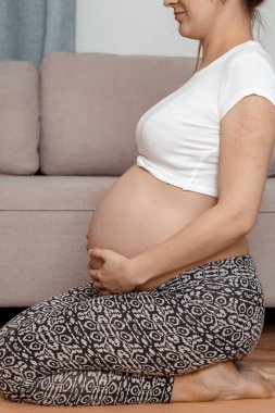 Güzel hamile kadın karnını tutarak oturuyor. Genç hamile kadın dizlerinin üstüne çöker..