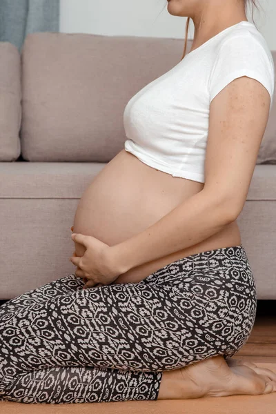 Güzel hamile kadın karnını tutarak oturuyor. Genç hamile kadın dizlerinin üstüne çöker..