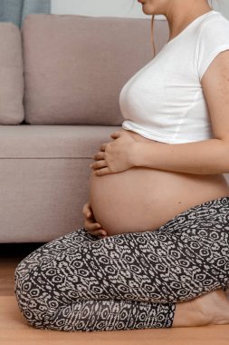 Güzel hamile kadın karnını tutarak oturuyor. Genç hamile kadın dizlerinin üstüne çöker..