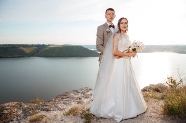 Pretty bride and stylish groom. Beautifull wedding couple embracing near the shore of a mountain river with stones. Wedding at Bakota.