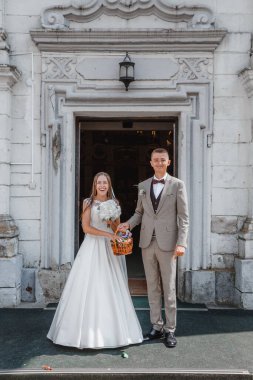 Happy wedding photography of bride and groom at wedding ceremony. The groom looks at the bride. Bride and groom holding hands, walk near the church after the wedding ceremony. Wedding day.
