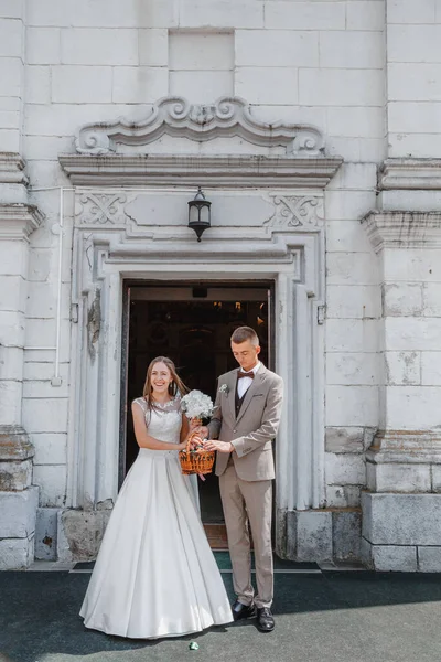 Happy wedding photography of bride and groom at wedding ceremony. The groom looks at the bride. Bride and groom holding hands, walk near the church after the wedding ceremony. Wedding day.