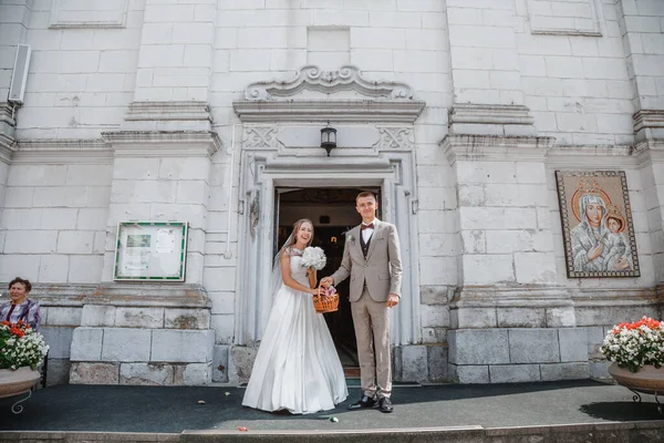 Happy wedding photography of bride and groom at wedding ceremony. The groom looks at the bride. Bride and groom holding hands, walk near the church after the wedding ceremony. Wedding day.