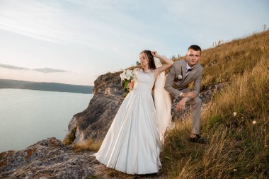 Pretty bride and stylish groom. Beautifull wedding couple embracing near the shore of a mountain river with stones. Wedding at Bakota.