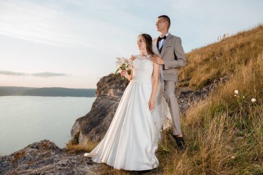 Pretty bride and stylish groom. Beautifull wedding couple embracing near the shore of a mountain river with stones. Wedding at Bakota.