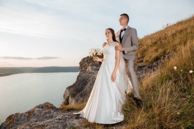 Pretty bride and stylish groom. Beautifull wedding couple embracing near the shore of a mountain river with stones. Wedding at Bakota.