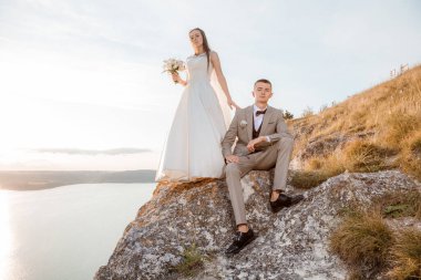 Pretty bride and stylish groom. Beautifull wedding couple embracing near the shore of a mountain river with stones. Wedding at Bakota.