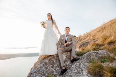 Pretty bride and stylish groom. Beautifull wedding couple embracing near the shore of a mountain river with stones. Wedding at Bakota.